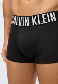 Närbild av en person som bär svarta Calvin Klein kalsonger med en synlig logotyp på midjebandet.