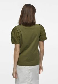 Olivgrön t-shirt med korta, texturerade puffärmar. Huvuddelens material är slätt och enfärgat, medan ärmarna har ögondetaljer.