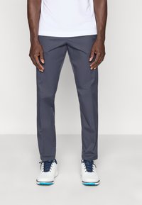 Pantalones de golf grises con textura suave, diseño entallado y bolsillos laterales, combinados con zapatos de golf blancos con cordones azules.