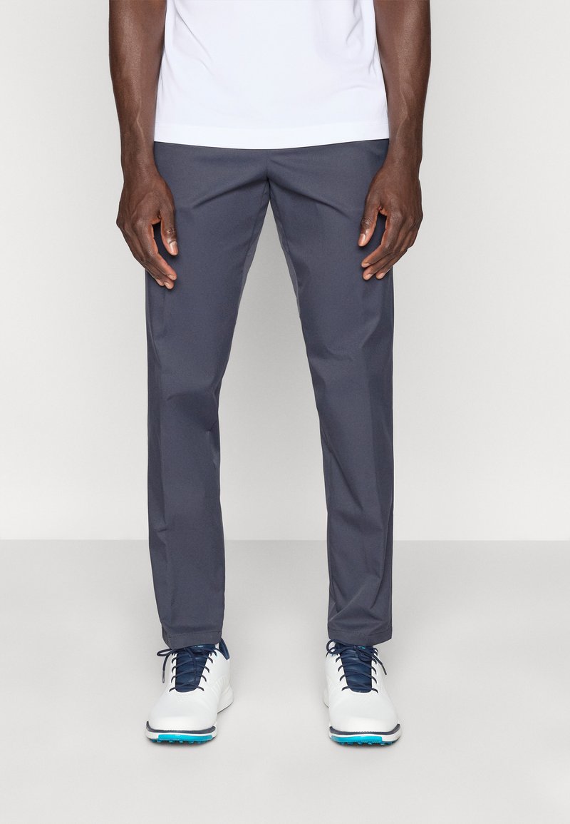 Pantalones de golf grises con textura suave, diseño entallado y bolsillos laterales, combinados con zapatos de golf blancos con cordones azules.