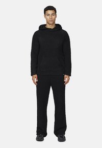 Felpa con cappuccio nera in pile con tasca frontale, abbinata a pantaloni in pile neri coordinati. Entrambi gli articoli hanno un aspetto morbido e texturizzato e una vestibilità comoda.