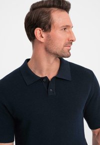 Marinblå kortärmad polo tshirt med texturerat mönster, knäppning och klassisk krage. Skräddarsydd passform med ribbade ärmslut.