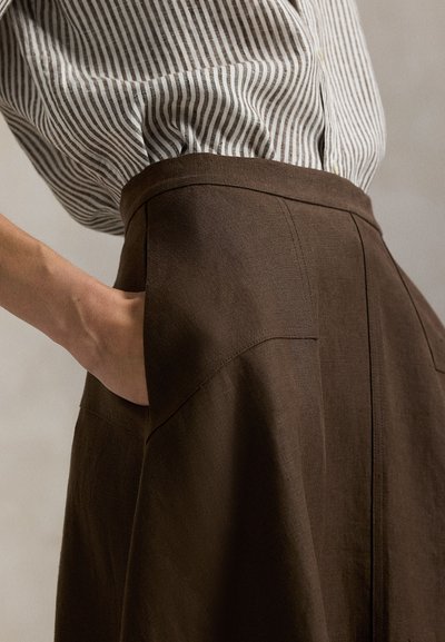 Καφέ λινή φούστα με ψηλή μέση και πλαϊνή τσέπη· συνδυασμένη με ριγέ πουκάμισο με κουμπιά· υφή υφάσματος σε κοντινή λήψη.
