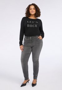Top negro de manga larga con letras de strass plateado "LET'S ROCK". Jeans grises con botones laterales, diseño ajustado y tacones negros puntiagudos.