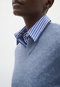 Modra volna pulover s krojem v črko V, preložen preko modro-belega okljuka s črtami. Opazen mehak tekstura in kontrastni vzorci.