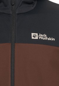 Giacca Jack Wolfskin con parte superiore nera e parte inferiore marrone scuro, dotata di una cerniera verticale e un logo sul petto.