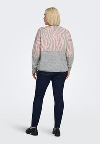 Grijze trui met lichtroze zebrapatroon op de achterkant, met een losse pasvorm en een geribde zoom, gecombineerd met donkere jeans en zwarte schoenen.