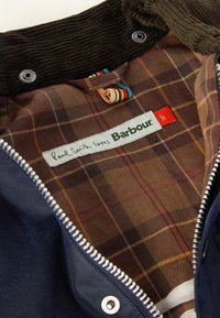 Ναυτικό σακάκι με κολάρο από βελούρ; καφέ καρό επένδυση με κόκκινες και κίτρινες τετράγωνες πινελιές; οι ετικέτες αναφέρουν "O Paul Smith αγαπά τον Barbour."