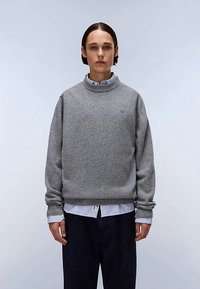 Gray sweatshirt with a round neck, textured fabric, ribbed cuffs, worn over a blue and white striped shirt, paired with dark pants.