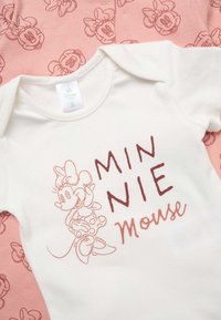 Body bianco per neonati con schizzo rosa di Minnie Mouse e testo, adagiato su tessuto rosa stampato con volti ripetuti di Minnie Mouse.