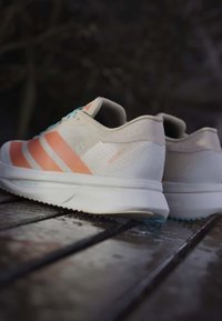 Pair of white and orange Adidas running shoes with blue laces resting on a wooden surface outdoors.