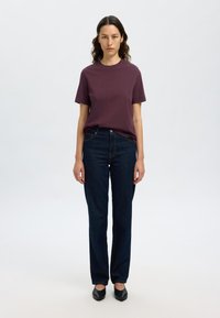 T-shirt bordeaux a girocollo abbinata a jeans dritti blu scuro. Scarpe nere chiuse. Design semplice e minimale con linee pulite.