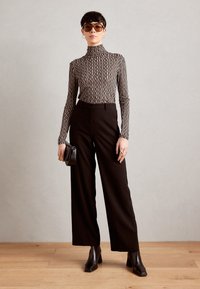 Schwarze hoch-taillierte weit geschnittene Hose, kombiniert mit einem eng anliegenden, beigen Rollkragenpullover mit Streifen und klobigen, mit Absatz versehenen Stiefeletten. Accessoires umfassen Sonnenbrille und eine Tasche.