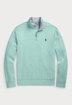Pull-over zippé court en vert menthe clair en tissu doux, avec un col intérieur gris, des poignets côtelés et un petit logo bleu sur la poitrine.