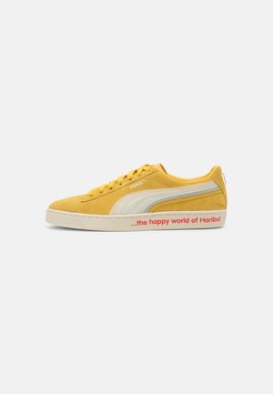 Baskets jaunes Puma avec une bande blanche, semelle en caoutchouc avec texte rouge "le monde heureux d'Haribo", et fermeture à lacets.