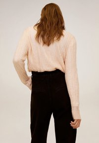 Pull en maille texturé, rose clair, avec une coupe ample et des manches longues, associé à un pantalon noir taille haute. Vue de dos présentée.