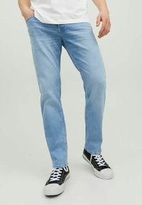 Jeans de denim azul claro con un corte recto, diseño de cinco bolsillos y un desgaste sutil. Combinados con zapatillas negras y blancas.