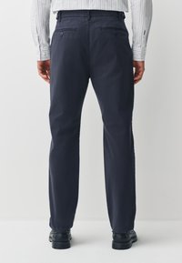 Pantalon marine en mélange de coton, doté d'une coupe droite, de poches arrière avec boutons, et d'une texture lisse.