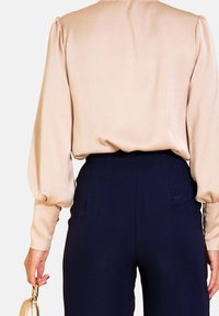 Blusa de satén beige de manga larga con hombros abullonados, combinada con pantalones navy ajustados. Bolso de mano con clasp de hardware dorado.