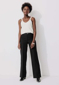 Pantalons noirs taille haute avec une coupe droite, associés à un haut léger sans manches présentant un motif texturé.