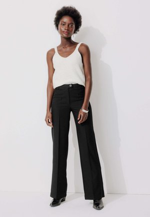 Pantalons noirs taille haute avec une coupe droite, associés à un haut léger sans manches présentant un motif texturé.