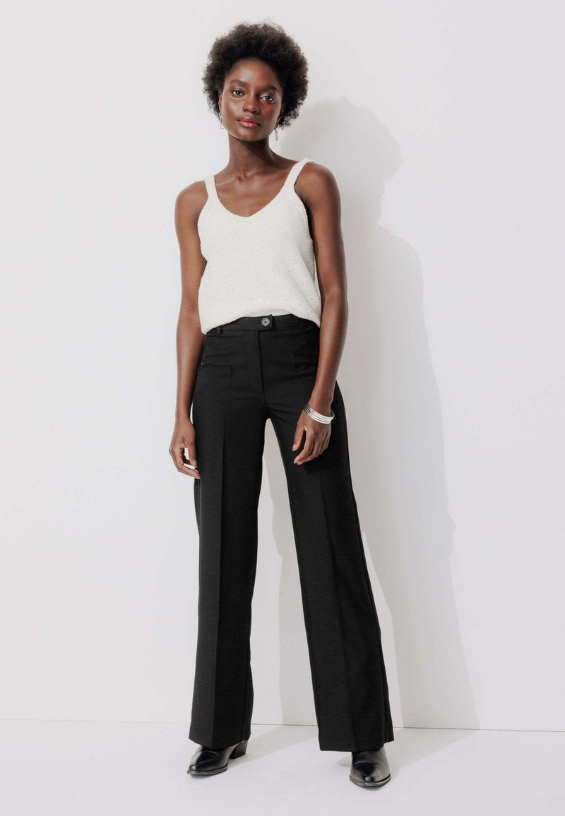 Pantalons noirs taille haute avec une coupe droite, associés à un haut léger sans manches présentant un motif texturé.