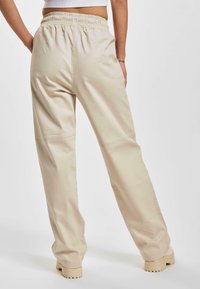 Pantaloni bej din amestec de bumbac, cu o croială relaxată, prevăzuți cu un tiv elastic și picioare drecte. Materialul are o textură netedă.