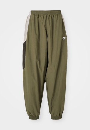 Pantaloni de trening Nike de culoare verde măsliniu cu talie și mansete elastice. Au panouri laterale în nuanțe de gri deschis și gri închis cu detalii ale logoului.