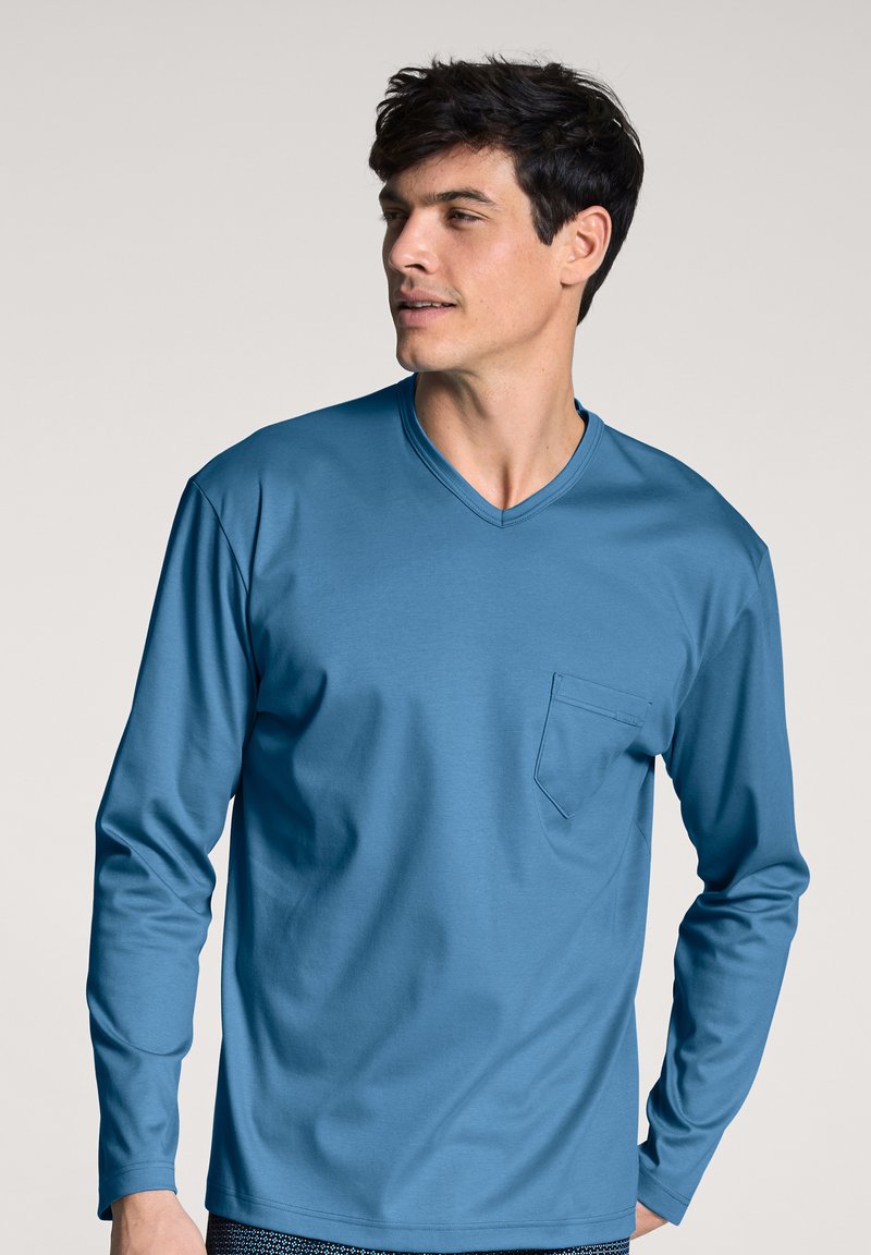 Long-sleeve V-neck shirt in solid blue, made from soft fabric. Features a single chest pocket and a relaxed fit. Smooth texture.