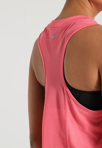 Top da allenamento rosa in tessuto a rete, con scollo a barchetta e un piccolo logo grigio vicino al collo. Testurizzato e leggero.