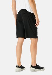 Sorte atletiske shorts lavet af letvægtsstof, med en elastisk talje og en afslappet pasform, parret med sorte sneakers.