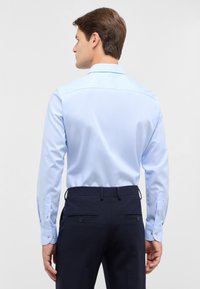Lichtblauwe overhemden met een gladde textuur, puntige kraag en knoopmanchetten, gecombineerd met donkere broek met achterzakken.
