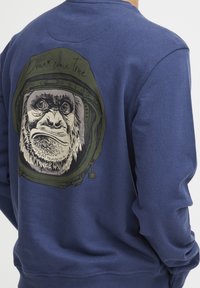 Navy blue sweatshirt featuring a graphic of a gorilla in a space helmet on the back, with the text "Dream come true" above the illustration.