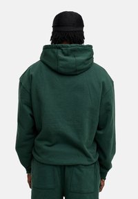 Dunkelgrüner Hoodie mit großer Kapuze, lockerer Passform und gerippten Bündchen. Aus Baumwollmaterial mit weicher Textur, kombiniert mit passender Hose.