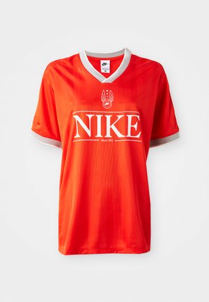 Maillot Nike rouge avec un col en V, bord gris sur les manches, et un grand logo "NIKE" blanc. Tissu lisse et léger avec un motif rayé subtil.
