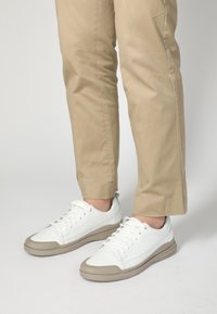 Hvide lædersneakers med lav profil, gummibezige sål og grå accenter. Snørebånd, der er bundet, og syning detaljer på siderne.