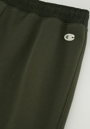 Pantalones deportivos de color verde oscuro con cintura elástica, tejido texturizado y un pequeño logo bordado en el muslo izquierdo inferior.