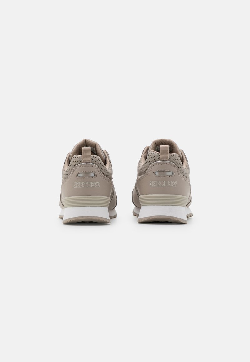 Par de zapatillas Skechers beige visto desde atrás, con tiradores, parte superior perforada y suelas intermedias blancas sobre un fondo liso.