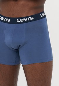Kék boxer alsó, pamutból készült, sötét derékpánttal, fehér "Levi's" logóval. Simaság, testhezálló dizájn és combközépig érő takarás.