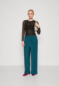Sort mesh langærmet top, teal plisserede viddebukser, lyserøde spidse sko og en sølvfarvet tekstureret clutch. Enkle accessories.
