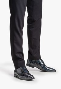Scarpe nere eleganti con una finitura lucida, caratterizzate da un motivo luccicante blu e argento, completate da lacci neri e un design a punta.