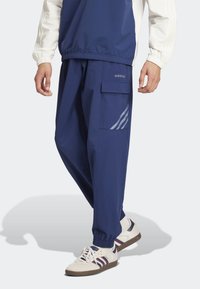 Námořnické modré cargo kalhoty vyrobené z lehké tkaniny s elastickými manžetami, boční kapsou a šedým trojpruhovým detailem na stehně.