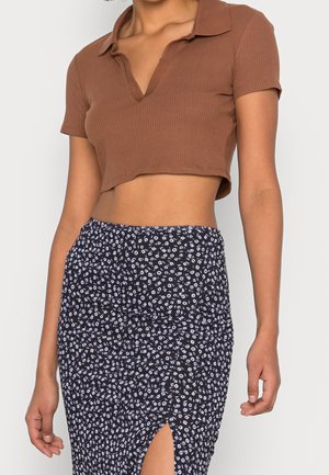 Hnědá žebrovaná krátká polokošile s krátkými rukávy ve spojení s černou sukní s květinovým potiskem a bočním rozparkem.