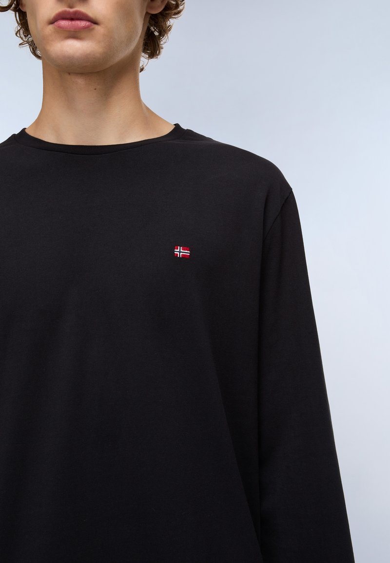 Schwarzes Langarm-T-Shirt mit rundem Halsausschnitt und einer kleinen rot-weißen norwegischen Flagge, die auf der Brust aufgestickt ist. Weicher Stoff.