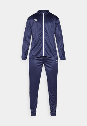 Marineblå træningsdragt lavet af glat, let materiale. Har en zip-up jakke med ståkrave og matchende bukser, logo på begge dele.