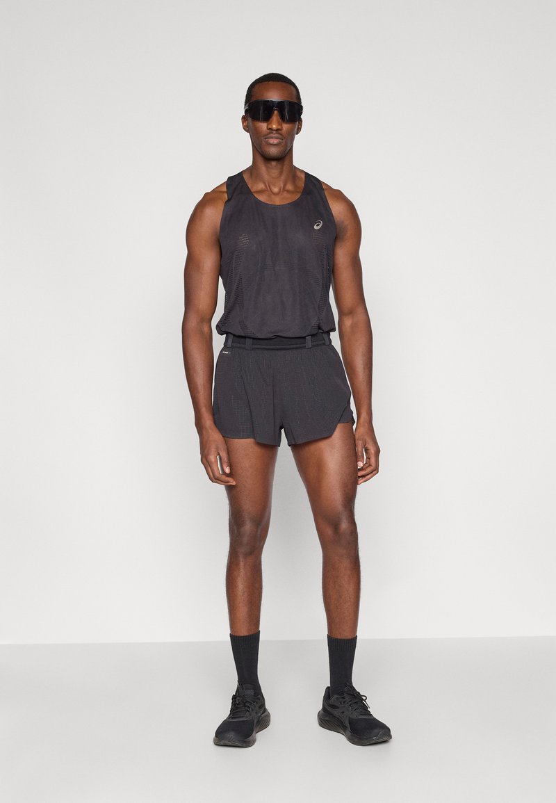 Débardeur de sport noir en tissu texturé avec logo, associé à un short assorti. Porté avec des chaussettes et des chaussures noires, ainsi que des lunettes de soleil foncées.