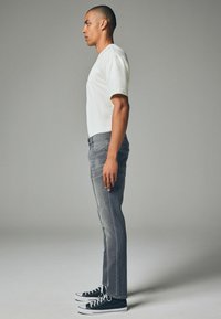 Jeans gri cu o croială ajustată, din material de bumbac, cu buzunare frontale și închidere cu nasture. Asortați cu un tricou alb cu mânecă scurtă și teniși negri.