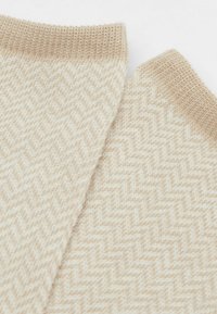 Beige mönstrad textil med en fiskbensdesign, med en mjuk textur och ribbade kanter, närbild som framhäver de intrikata detaljerna.