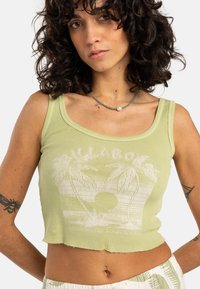 Light green ribbed crop top featuring a beach graphic with palm trees and sun. Scalloped hem, round neckline, and slim fit design.