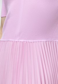 Κοντινή λήψη ενός ροζ φορέματος που δείχνει ριμπ πλεκτό κορσέ και πλισέ φούστα με κοντό μανίκι στην αριστερή πλευρά.